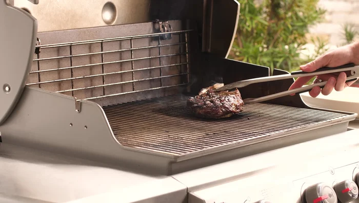 To finish cooking and prevent burning, move the steak to a lower heat area of the grill, keeping the lid closed.
