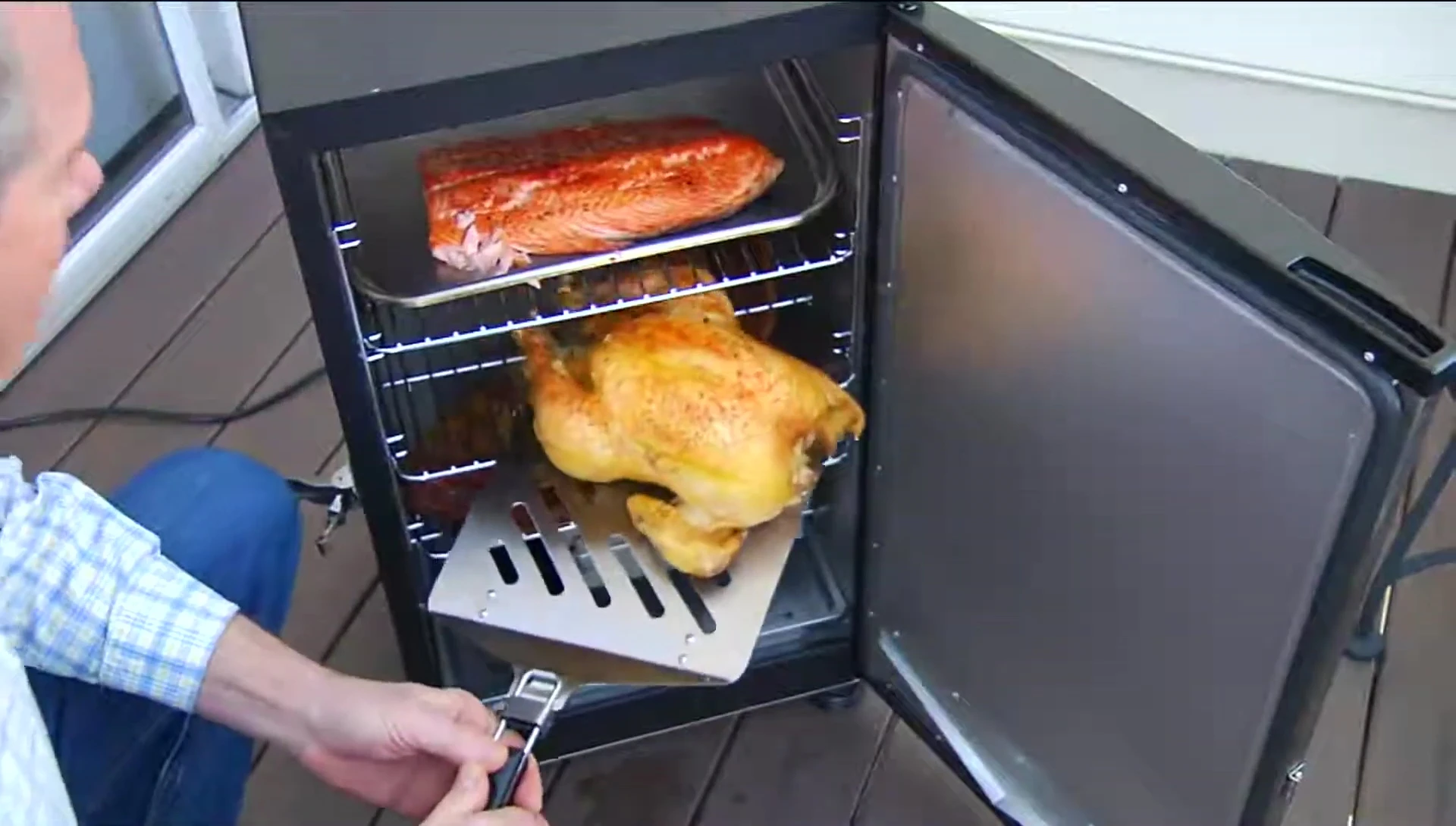 A whole roasted turkey being lifted from a smoker using the spatula.