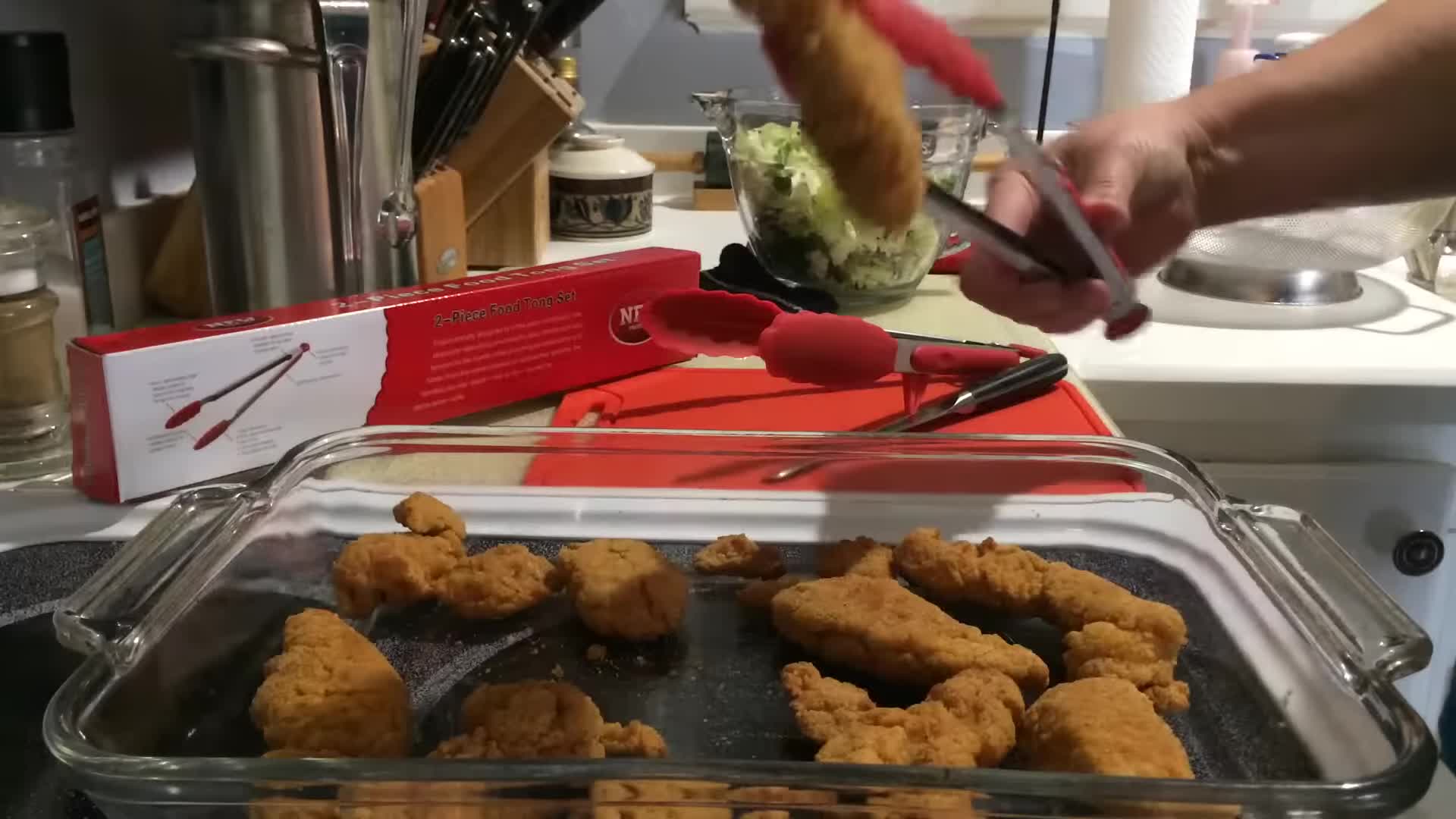 The tongs being used to lift a chicken from a baking tray.