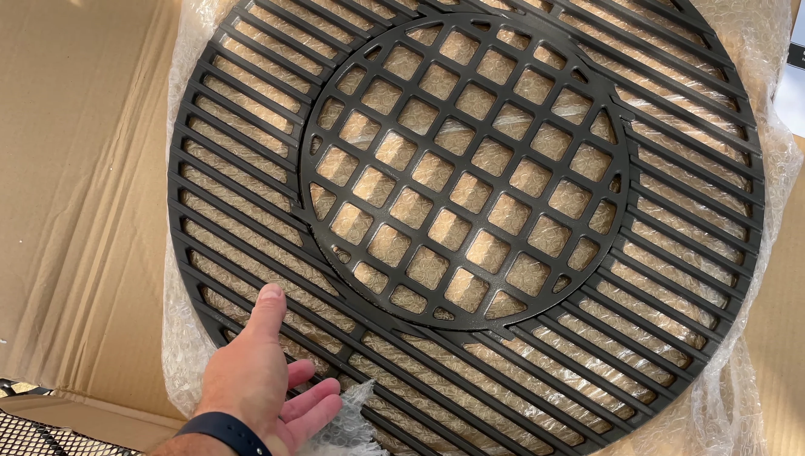 The cast iron grill grate in its packaging, showing the outer box and styrofoam protection.