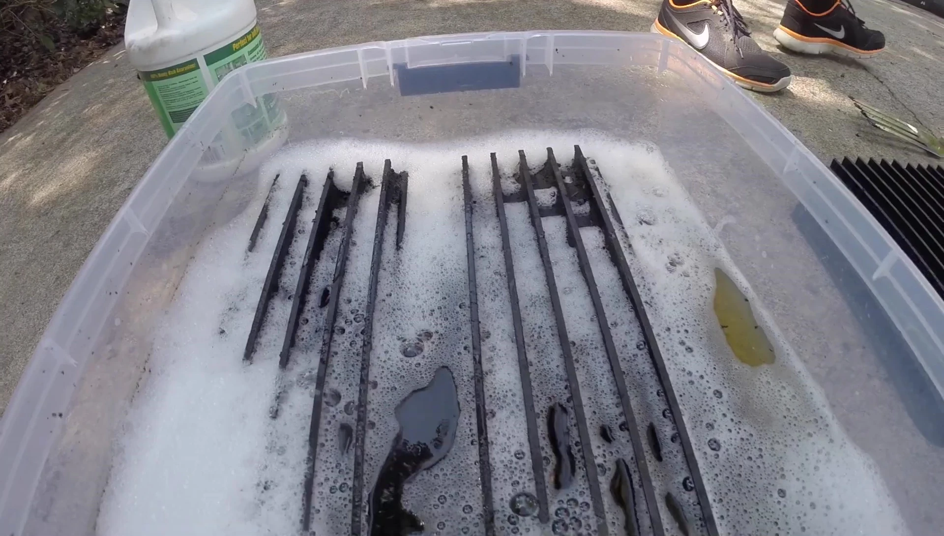 The grill grates being placed in a tub of Simple Green solution.