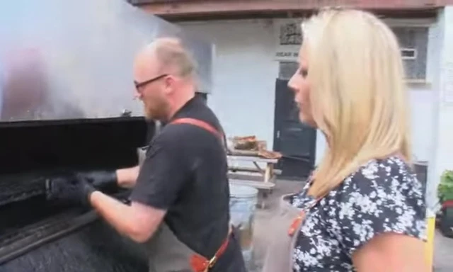 The wooden shovel being used to clean the grill grates.