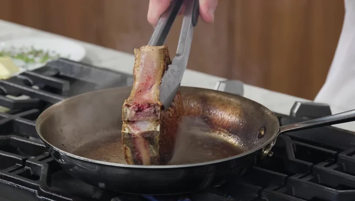 Once browned on both sides, sear the pork chop fat-side down to render the fat and reduce moisture.
