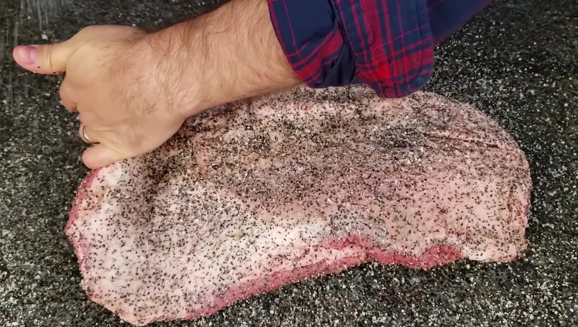 The presenter demonstrating how to generously apply the salt and pepper rub to the brisket.